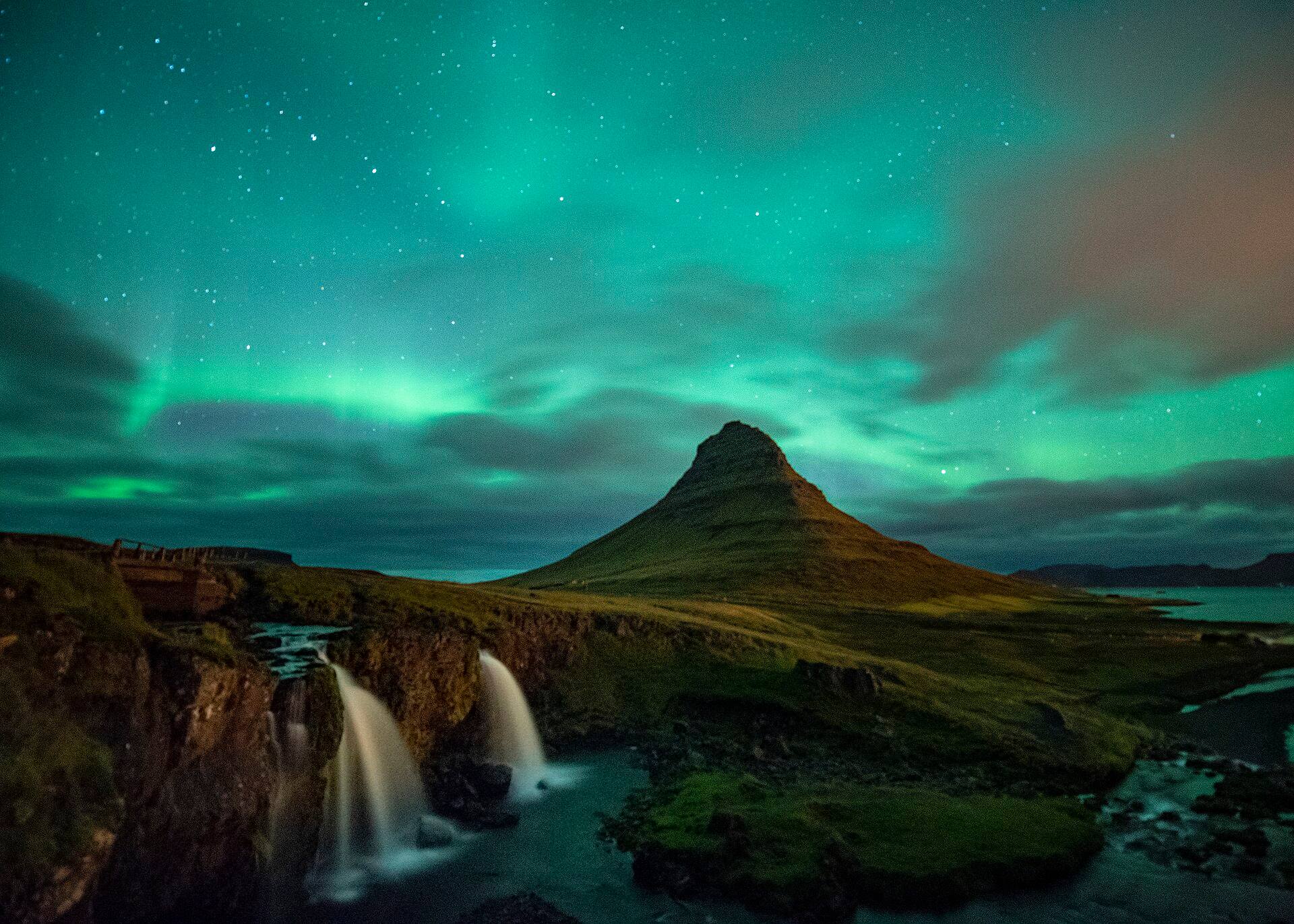 Grüne Nordlichter am Sternenhimmel über Kirkjufell und den Wasserfällen von Kirkjufellsfoss.